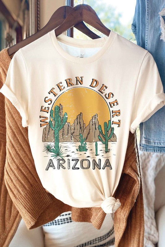 A person wearing the WESTERN DESERT ARIZONA Graphic Tee showcases a bold design featuring cacti and a mountainous landscape against a setting sun. With unisex sizing, this tee is perfect for anyone who loves desert vibes.