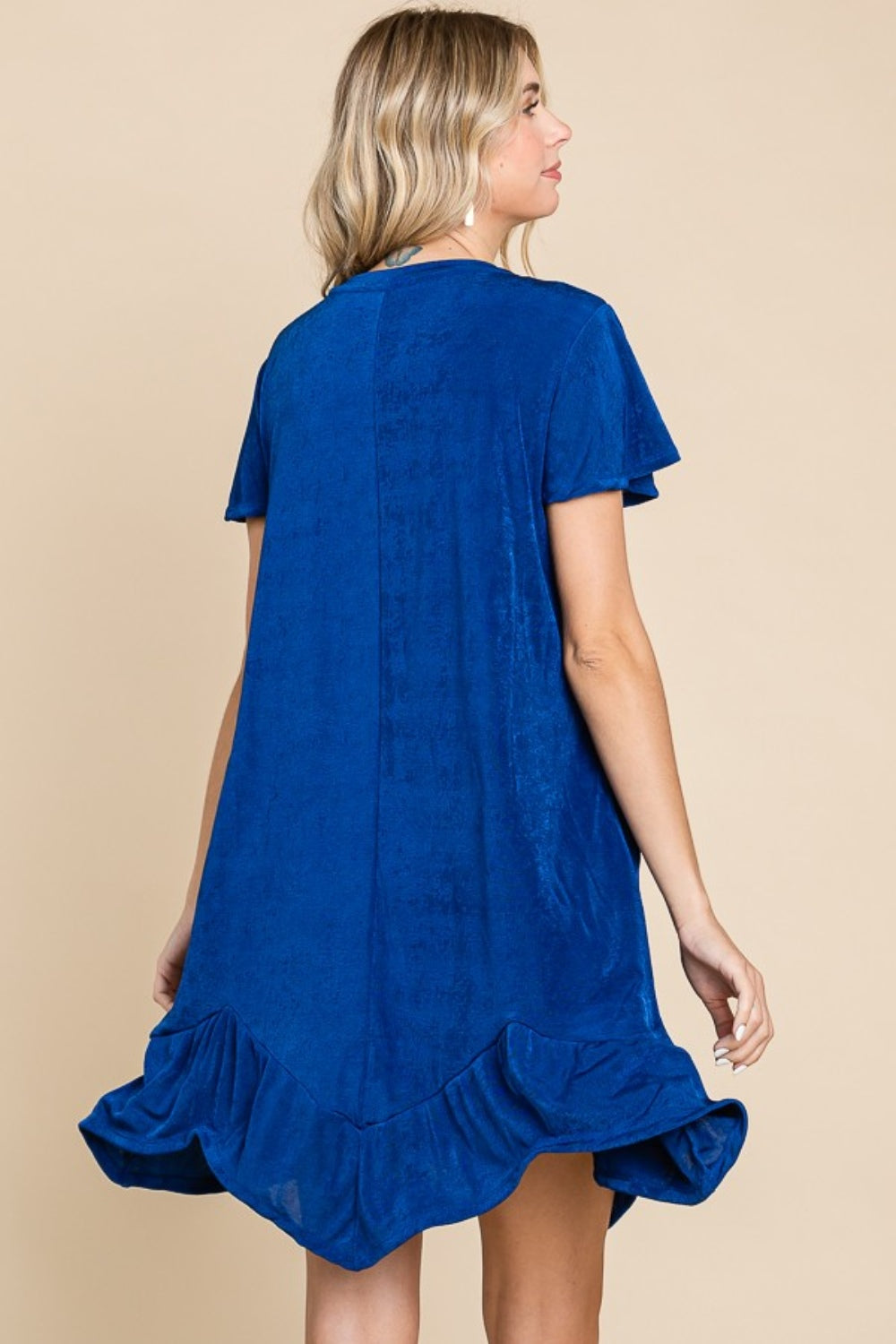 A woman wearing the Culture Code Full Size Short Sleeve Ruffled Asymmetric Hem Dress poses against a beige background.