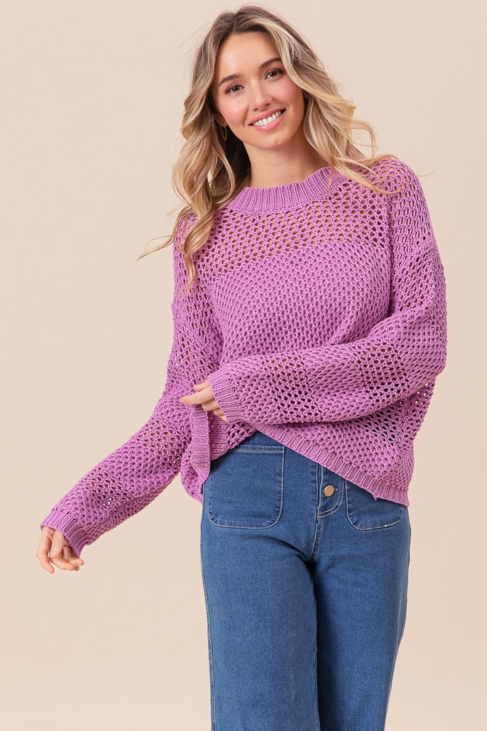 Wearing the BiBi Openwork Long Sleeve Knit Top in purple and blue jeans, a person smiles slightly while gazing to the side, exuding a fashion-forward vibe.