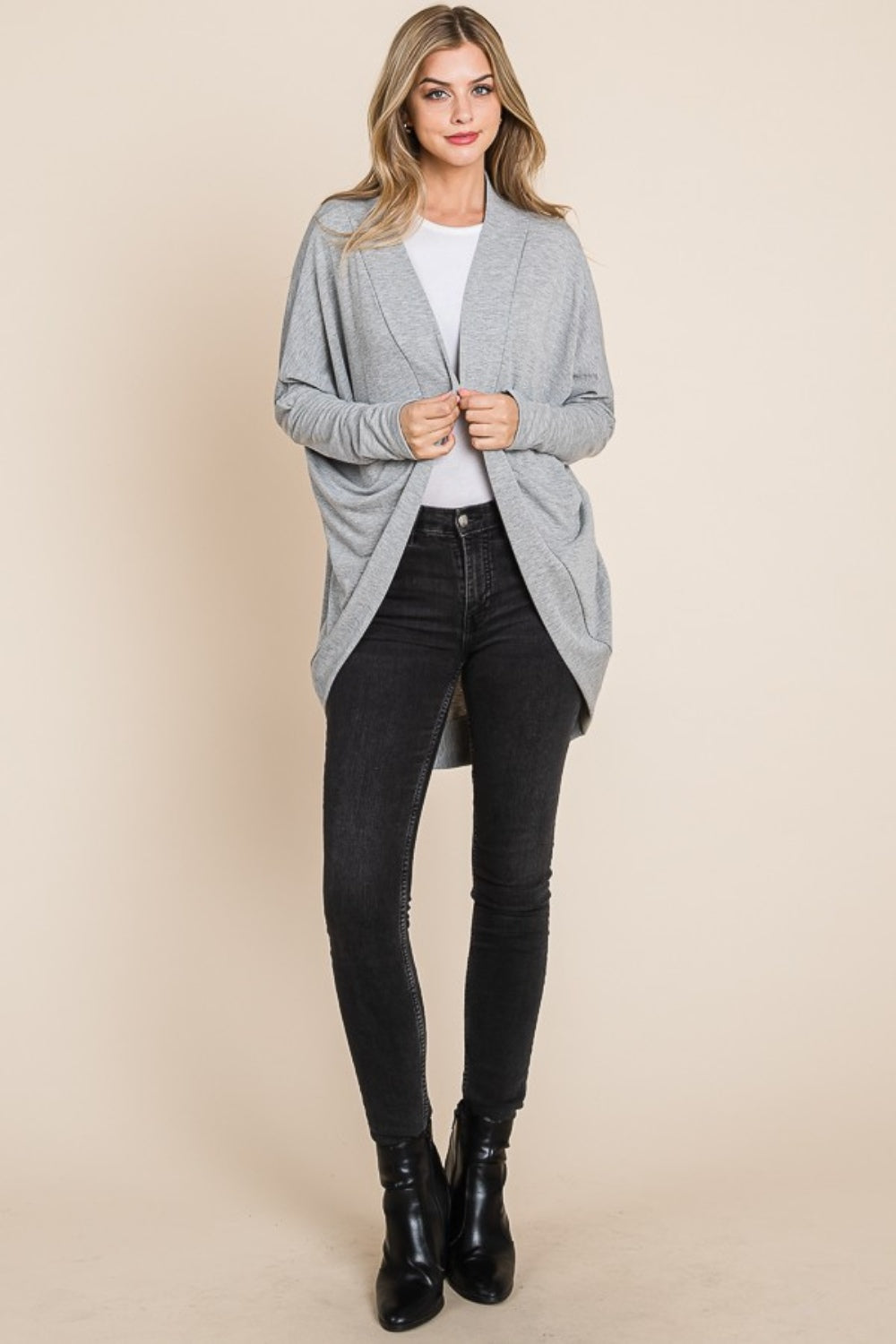 A woman wearing a white shirt, black jeans, and a versatile layering piece—the BOMBOM Open Front Long Sleeve Cocoon Cardigan in grey—stands against a plain beige background.