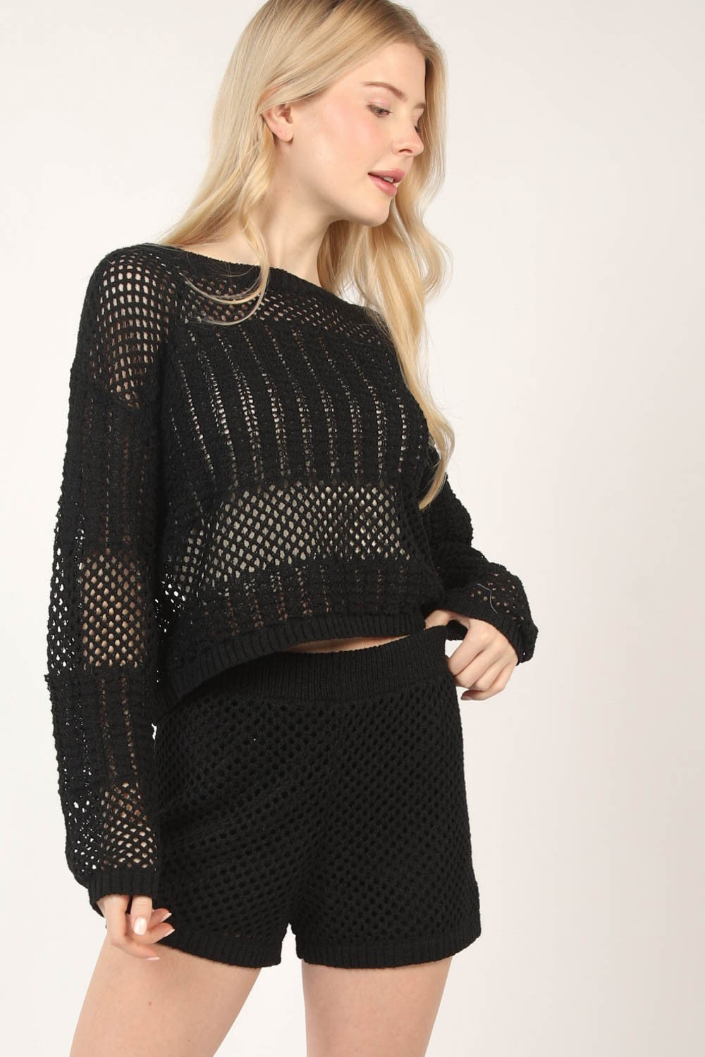 A person confidently stands against a plain background wearing the VERY J Openwork Cropped Cover Up and Shorts Set.