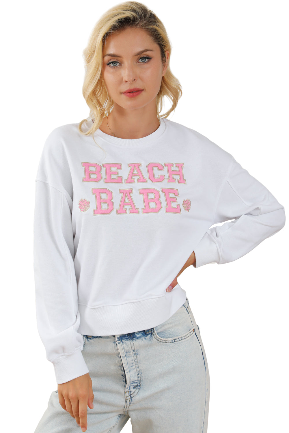 A person with long blonde hair is standing with their back to the camera, wearing a White BEACH BABE Slogan Graphic Casual Sweatshirt and light blue jeans.