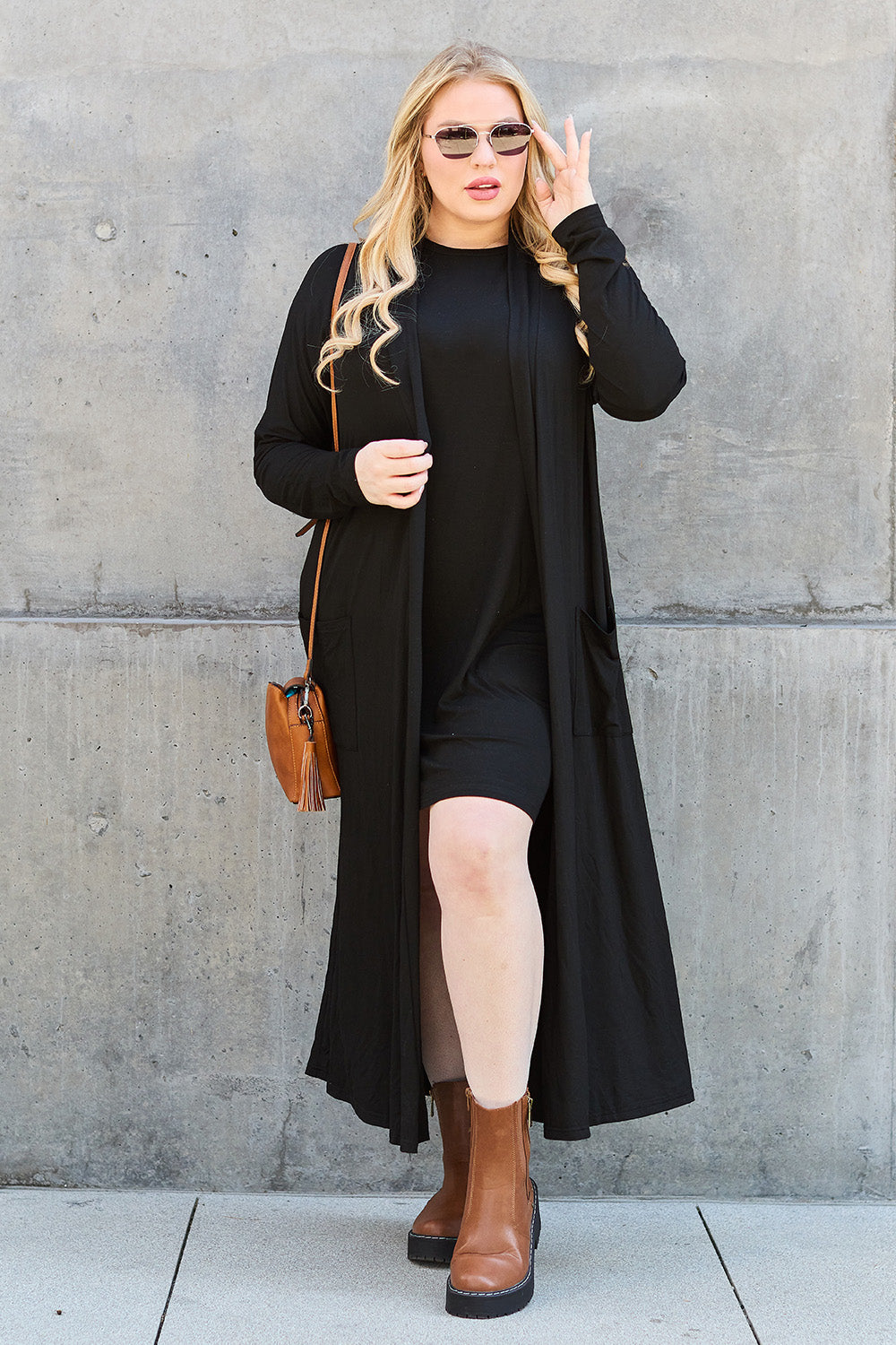 A woman stands against a concrete wall, wearing the Basic Bae Full Size Open Front Long Sleeve Cover Up made from rayon spandex, a white top, blue jeans in her perfect size, and brown shoes with her hands in her pockets. Machine wash cold for best results.