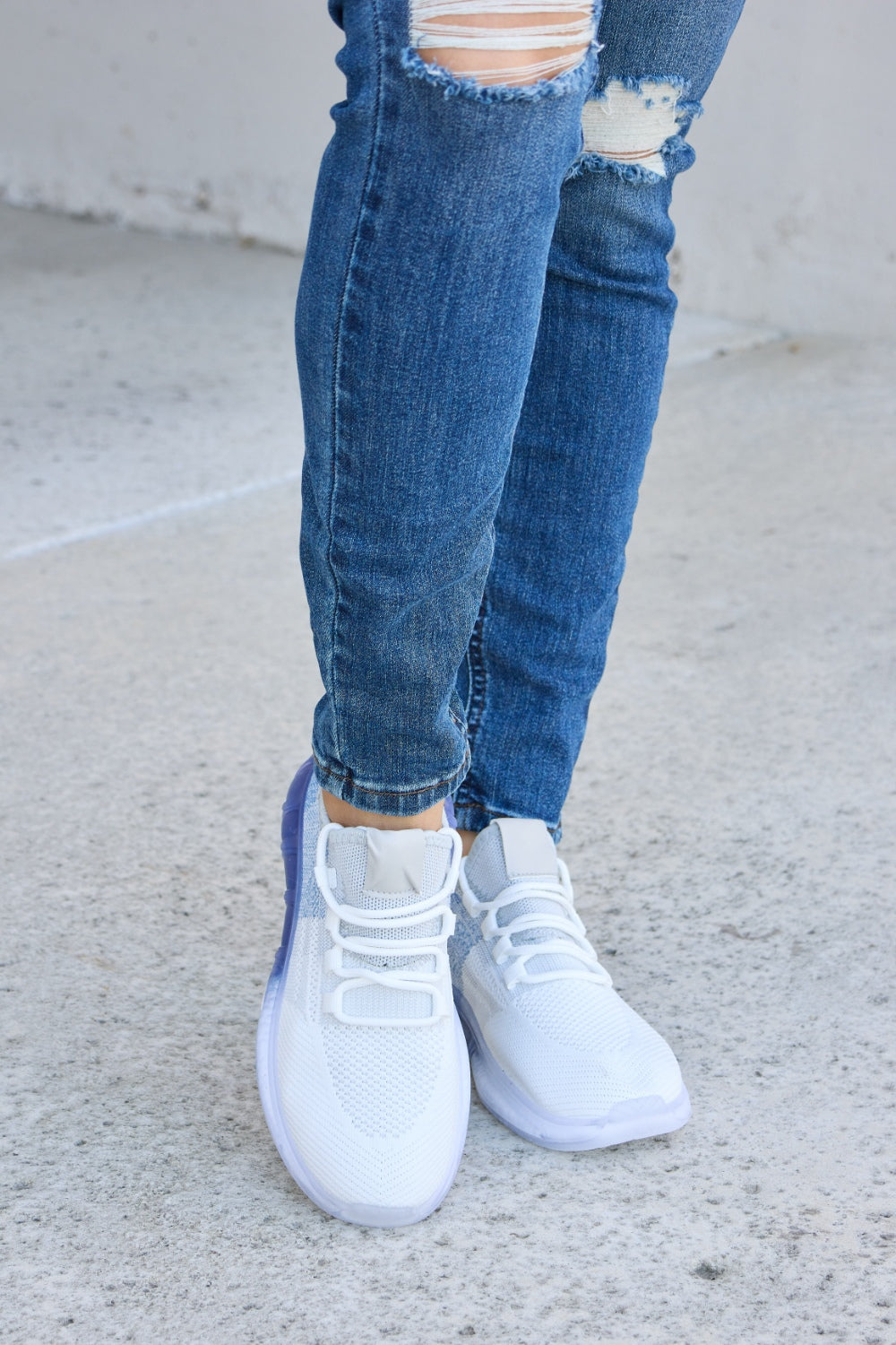 A person wearing distressed blue jeans and a pair of Forever Link Gradient Lace-Up Mesh Breathable Athletic Shoes, standing on a concrete surface.