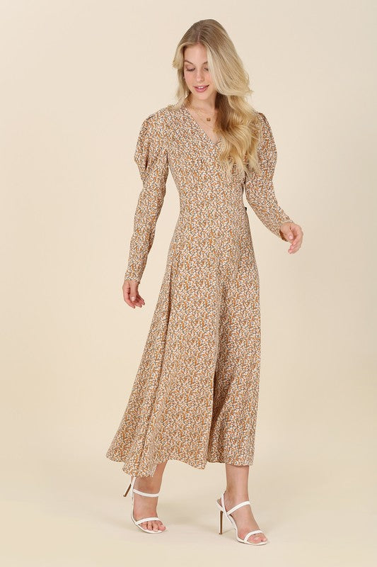 A woman gracefully poses against a beige background wearing the Fit and Flare floral maxi dress, featuring a V-neckline, elegant puff sleeves, and a complementary front slit.