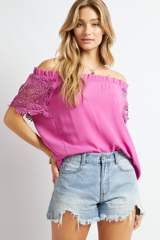 A woman in a bohemian-inspired Crochet Lace Sleeveless Accent Off Shoulder Top and white shorts stands indoors, looking to the side.