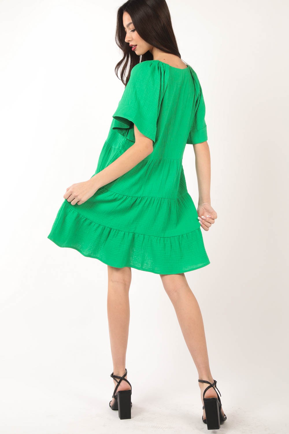 A woman poses against a white background, elegantly showcasing the flattering silhouette of the VERY J Texture V-Neck Ruffled Tiered Dress.