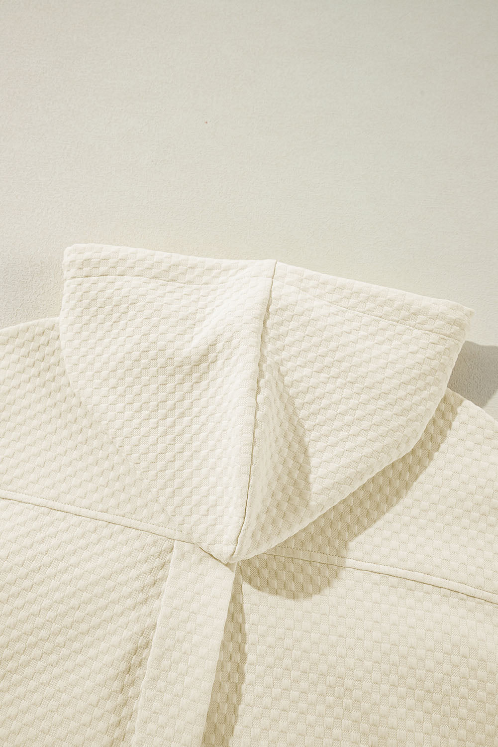 A person stands indoors facing away, wearing the Apricot Textured Buttoned Neckline Side Pockets Hoodie and black shorts. Their hand rests on their hip.