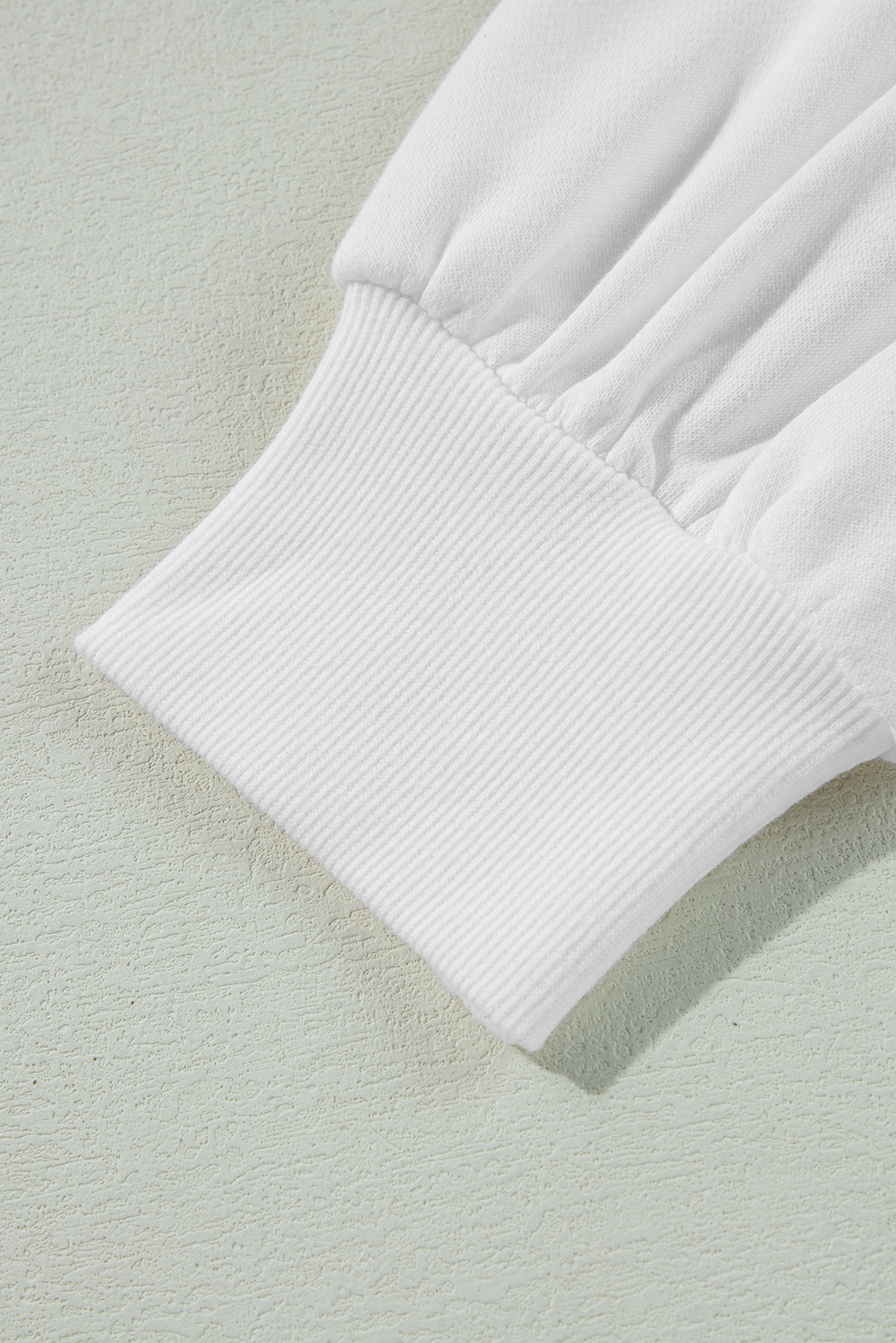 A person with long blonde hair is wearing a White BIRTHDAY QUEEN Graphic Balloon Sleeve Sweatshirt, paired with a pink feathered skirt, and sitting against a beautifully decorated backdrop.