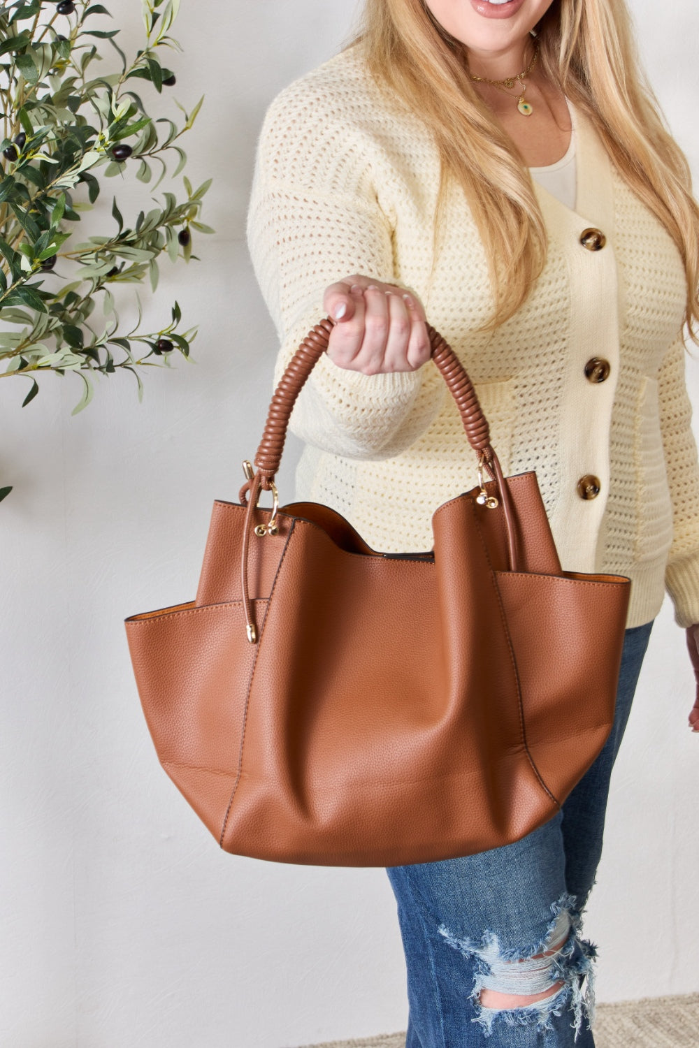 Effortlessly displaying the SHOMICO Faux Leather Handbag with Pouch, which features a spacious design in brown with gold accents and a woven handle, this piece exemplifies versatility. Paired with a cream sweater and blue jeans, its minimalist style perfectly balances fashion and function.