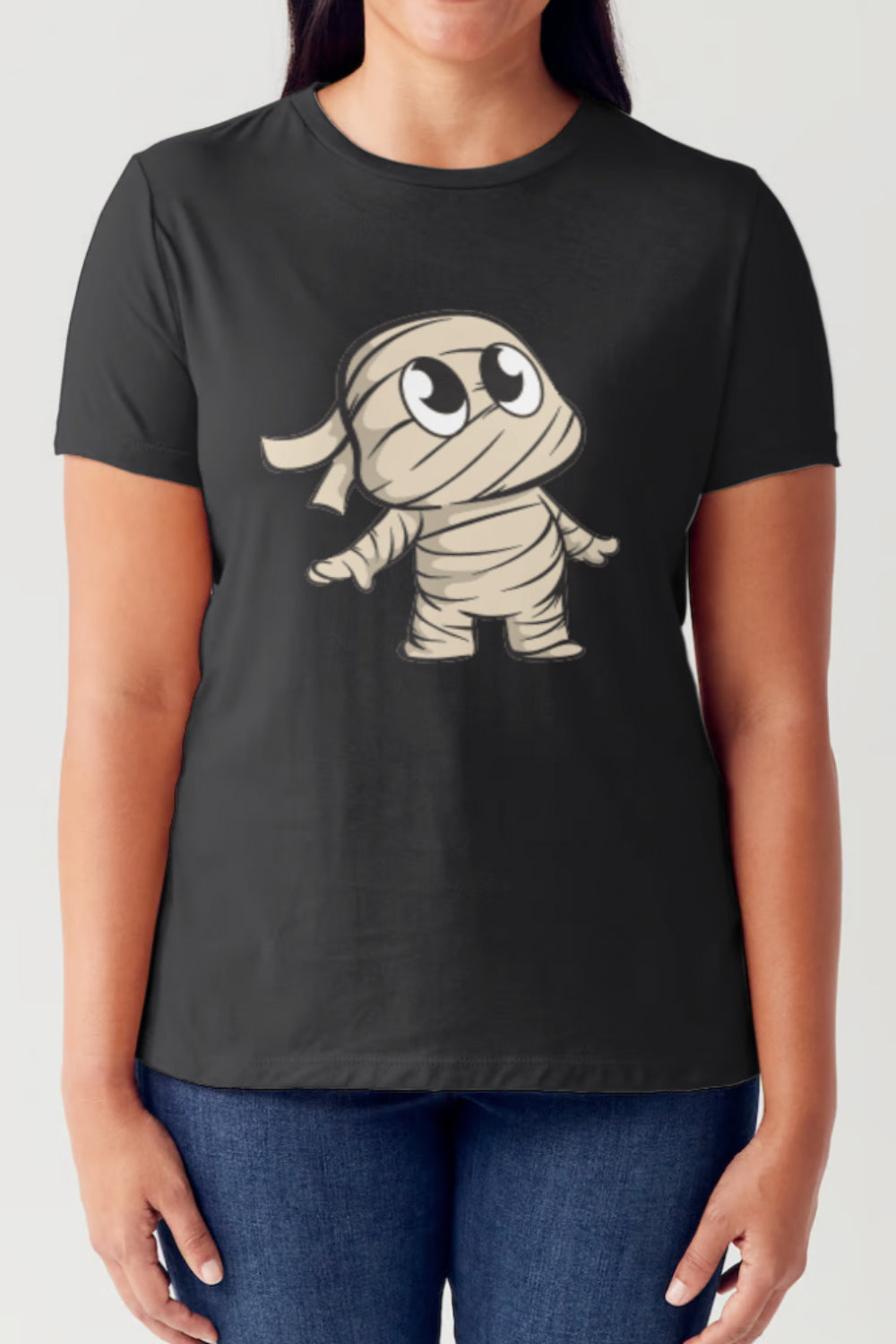 A person wearing a Simply Love Full Size Graphic Round Neck Short Sleeve Tubular T-Shirt, adorned with a cute cartoon character of a mummy on the front, stands with their arms relaxed by their sides. The white shirt fits comfortably and showcases its stylish design perfectly.