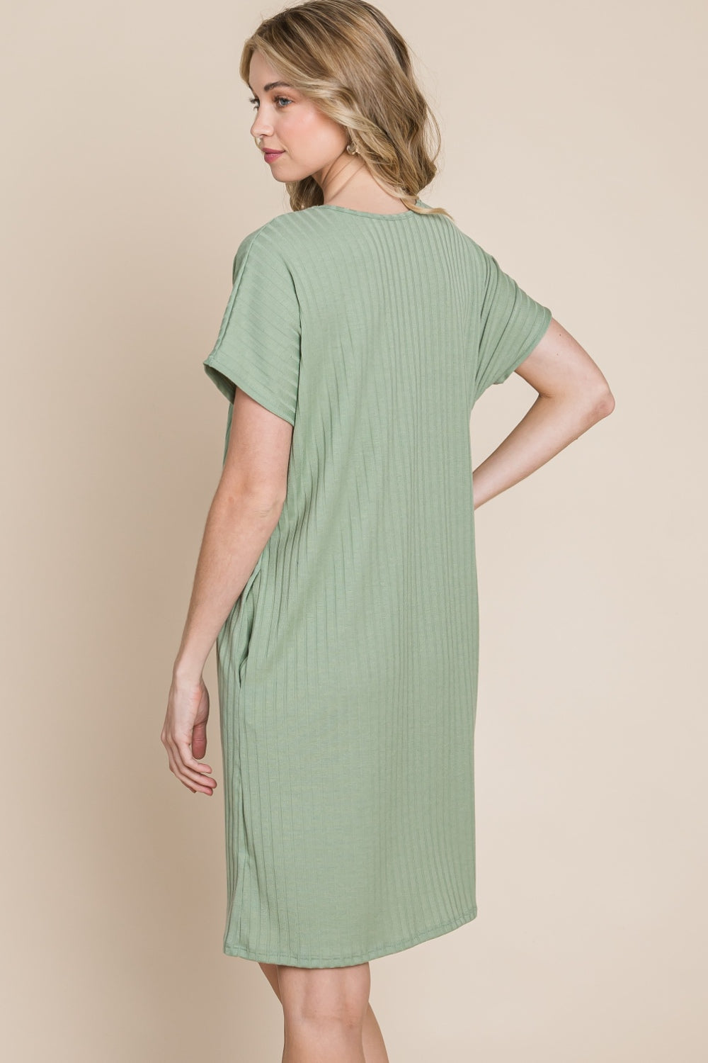 Against a beige background, a person is dressed in the BOMBOM Ribbed Round Neck Short Sleeve Dress in green, featuring a pocket.