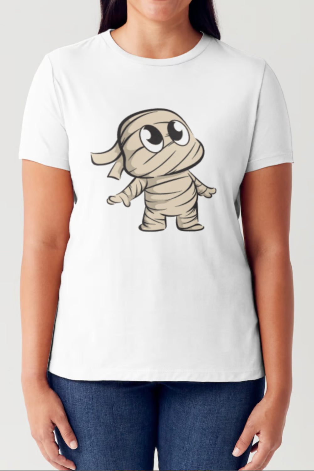 A person wearing a Simply Love Full Size Graphic Round Neck Short Sleeve Tubular T-Shirt, adorned with a cute cartoon character of a mummy on the front, stands with their arms relaxed by their sides. The white shirt fits comfortably and showcases its stylish design perfectly.