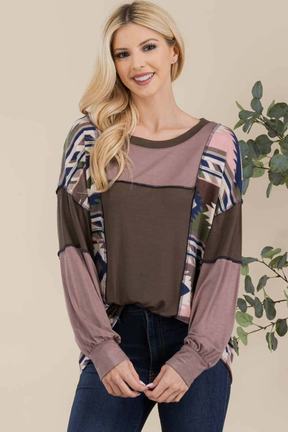 A woman with long blonde hair is wearing the Celeste Full Size Exposed Seam Printed Color Block T-Shirt and dark jeans, standing in front of a neutral background.