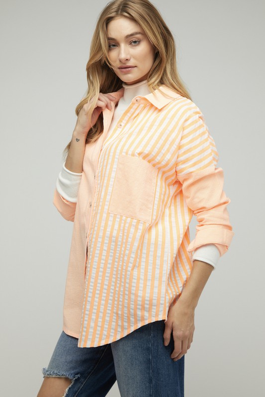 A person wearing a light pink Stripe Button Down Long Sleeve Shirt with rolled-up sleeves and jeans stands with their hands behind their head against a plain background.