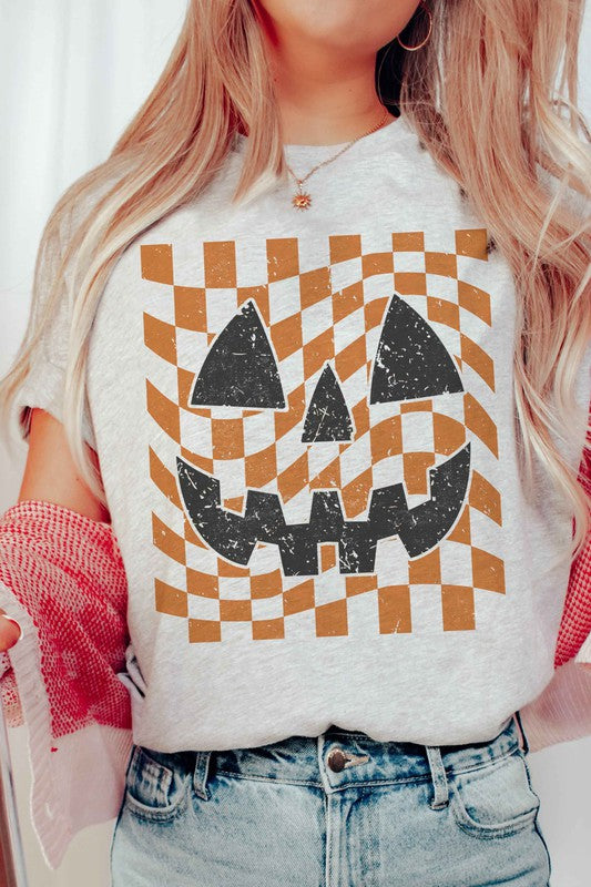 Person wearing a CHECKER PUMPKIN FACE Graphic Tee, made from 100% cotton, paired with high-waisted blue jeans.