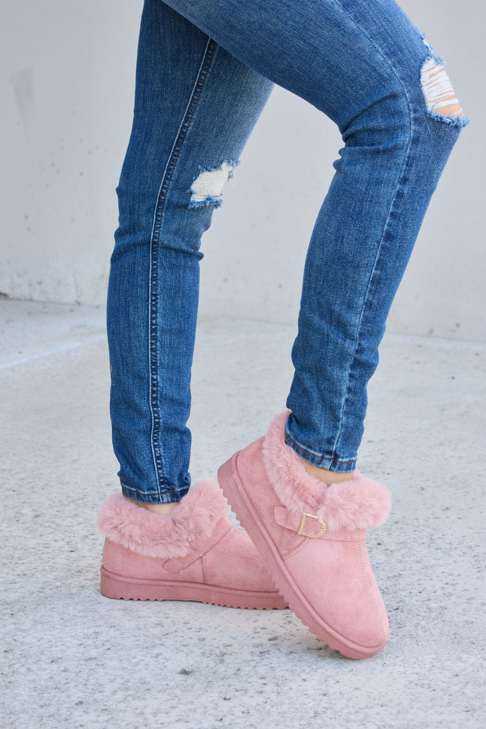 A person stands on a concrete surface, sporting ripped blue jeans and the Forever Link Furry Chunky Thermal Ankle Boots. The furry lining of these fashionable boots suggests both comfort and warmth for winter.