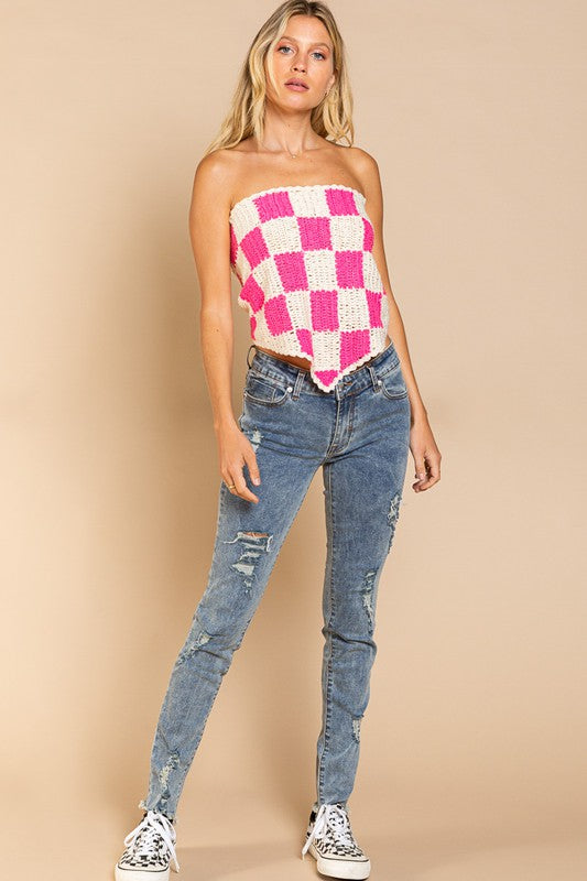 A woman stands against a beige background, wearing the playful Checkerboard Pattern Tube Top Sweater in pink and white, which beautifully contrasts with her blue jeans.