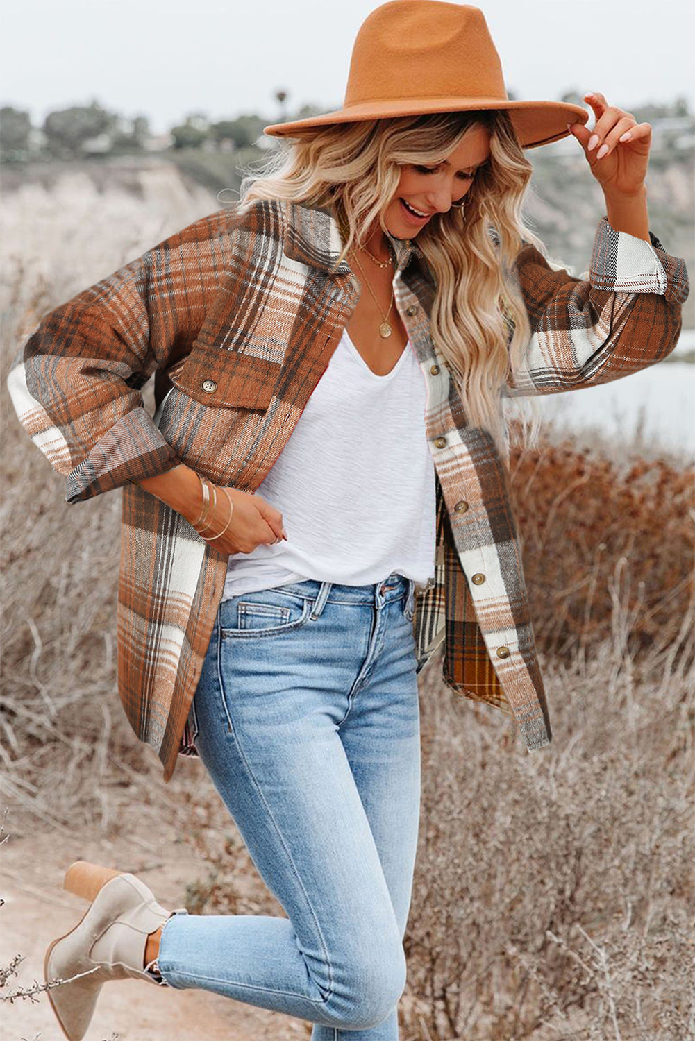 A woman wearing a white top, blue jeans, and the Gold Flame & Grey Plaid Button Up Collared Flannel Shacket smiles while posed outdoors.