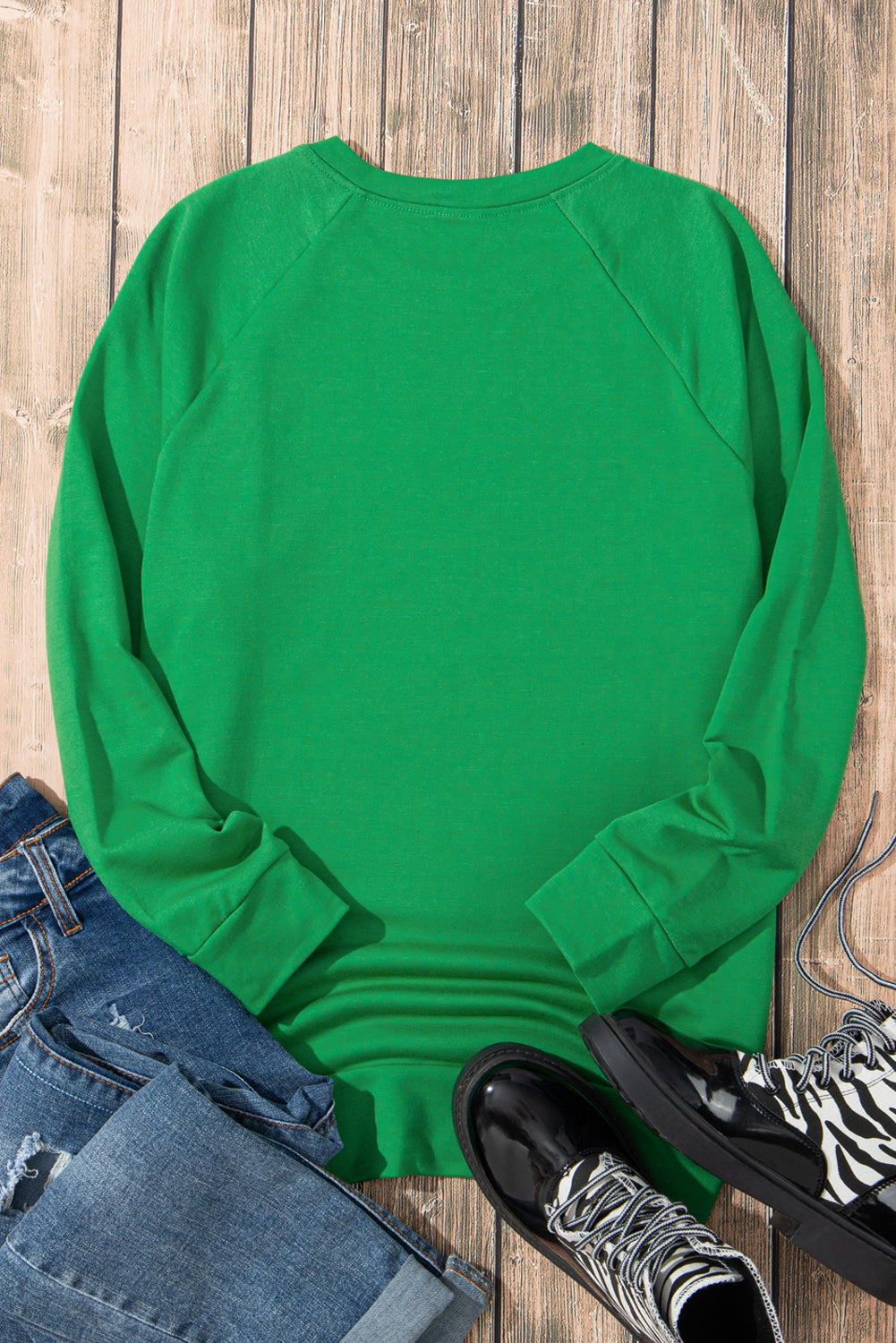 A person with wavy hair wearing a Green Solid Round Neck Raglan Sleeve Sweatshirt and blue jeans is standing with their back to the camera in front of white curtains.