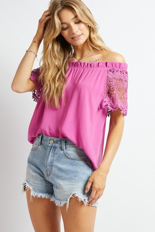 A woman in a bohemian-inspired Crochet Lace Sleeveless Accent Off Shoulder Top and white shorts stands indoors, looking to the side.