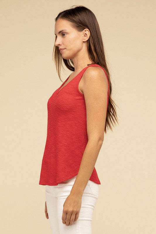 A woman in a stylish and adaptable V Neck Sleeveless Cami Top paired with jeans stands against a beige background. She has long brown hair and maintains a neutral expression.