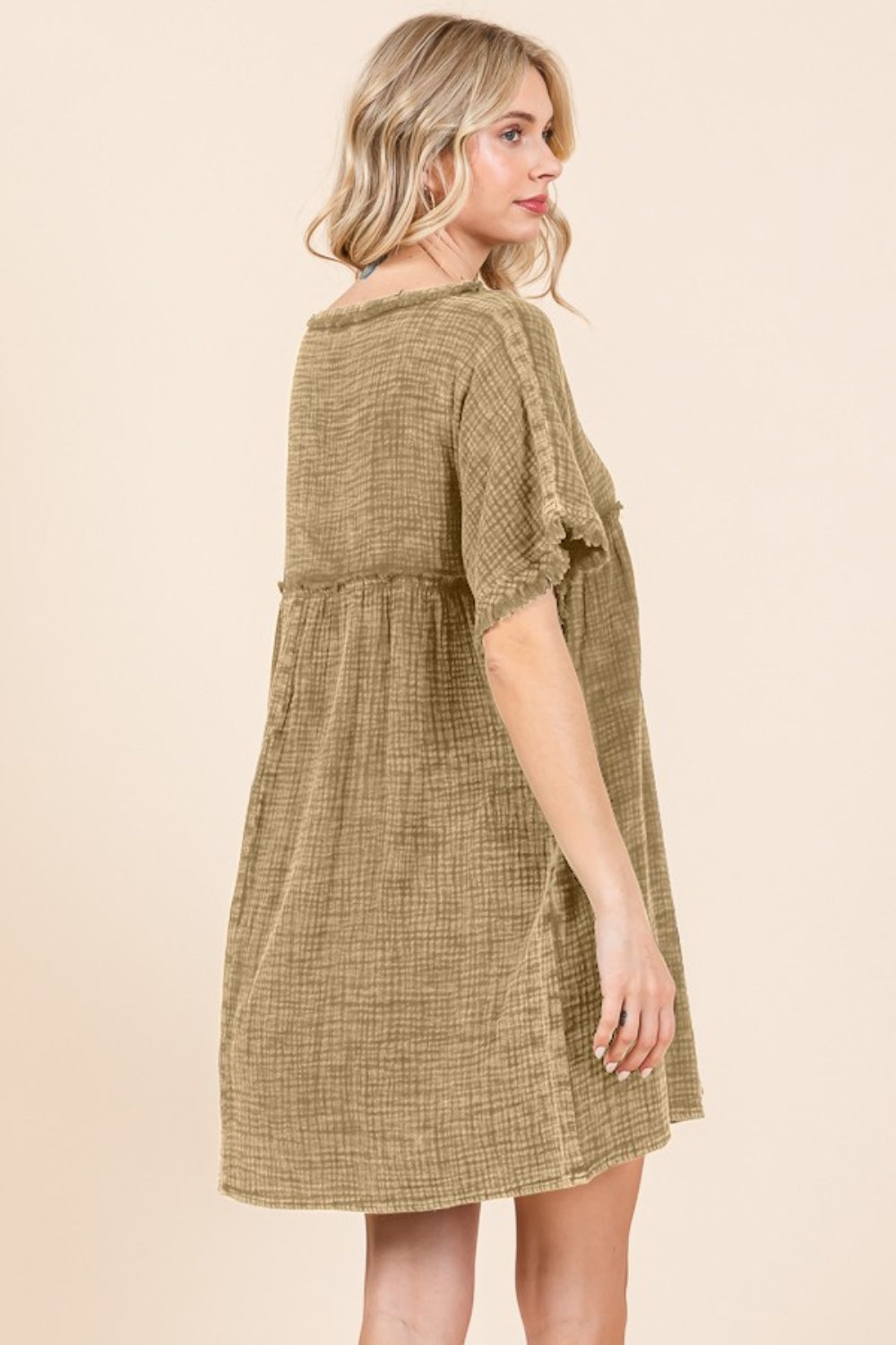 A person is wearing the Culture Code Full Size Short Sleeve Babydoll Texture Dress with Pockets, characterized by its loose fit and short sleeves, in a light brown shade, while standing against a plain background.