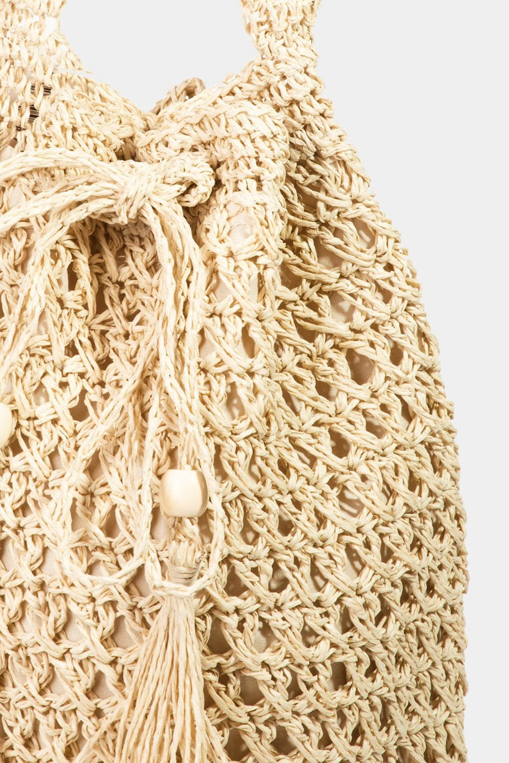 Fame Straw Braided Drawstring Tote Bag with Tassel in beige, highlighted by its crochet-like texture and a practical drawstring closure.