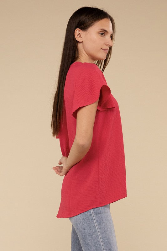 A woman with long straight hair models the Woven Airflow Flutter Sleeve Top in green, matched with light blue jeans, as she poses with her hands in her pockets against a plain beige background.