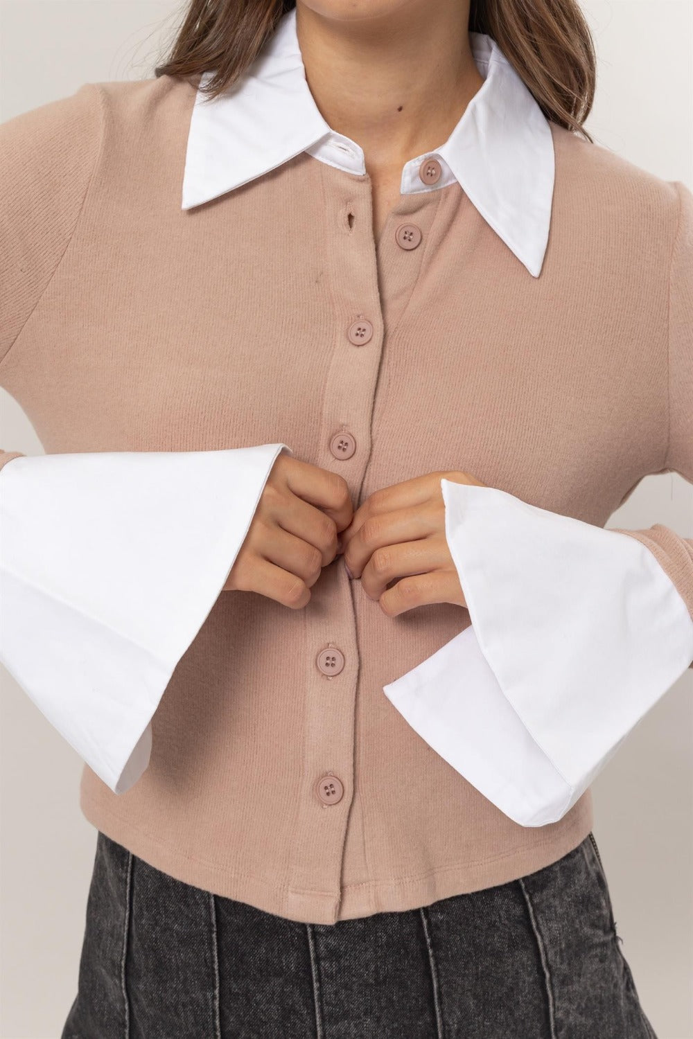 A woman stands wearing the HYFVE Collared Contrast Button Down Crop Knit Cardigan with white cuffs and collar, a dark pleated skirt, and black ankle boots. She poses with her hand on her hip in front of a plain background.