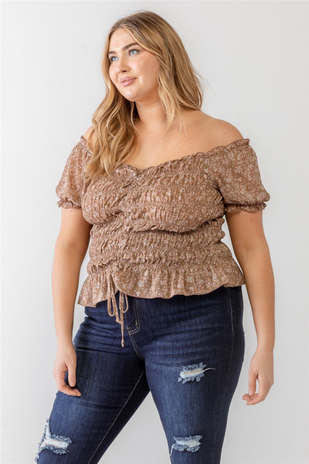 Wearing the Zenobia Plus Size Frill Ruched Off-Shoulder Short Sleeve Blouse and ripped jeans, a person with long hair poses against a plain white background.