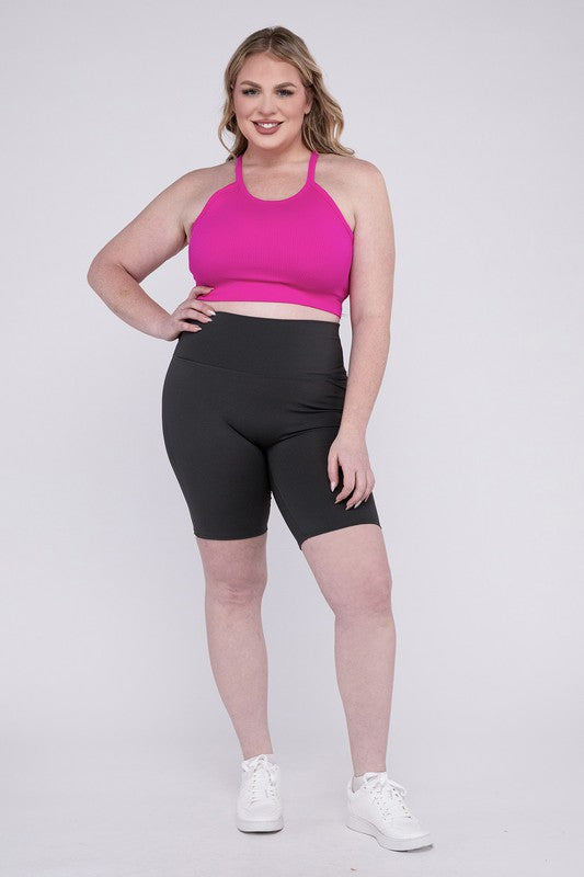 Against a plain background, a person showcases the Plus Athletic High Rise Biker Shorts in coral, crafted from high-quality athletic fabric and paired with a pink top.