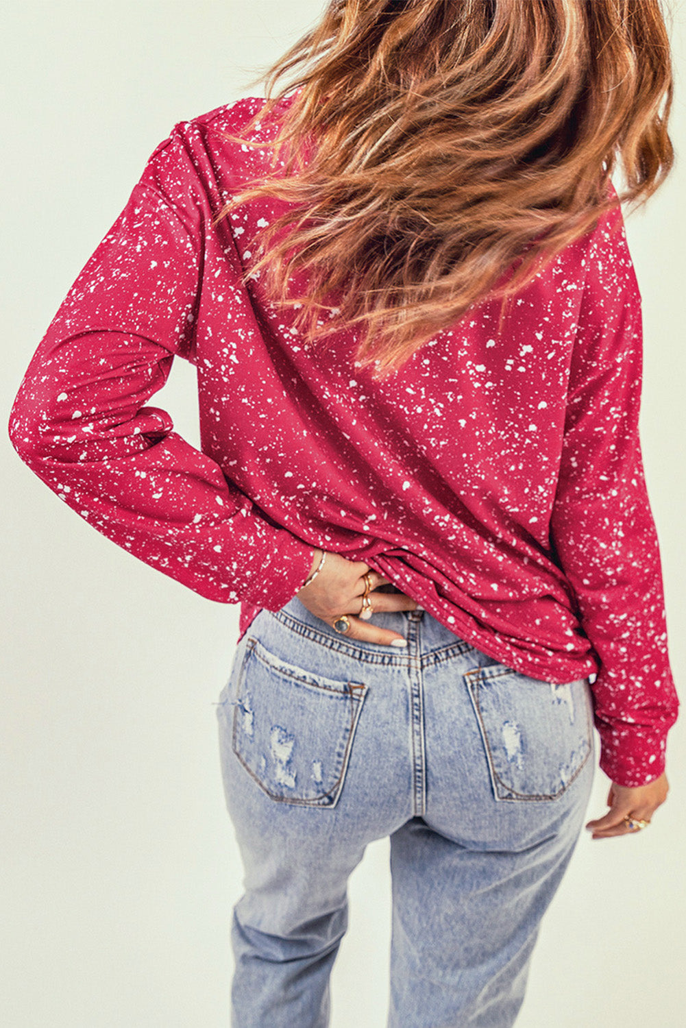 A person with long hair is facing away, wearing a casual Fiery Red Tie-dyed Crew Neck Pullover Sweatshirt and light blue distressed jeans.