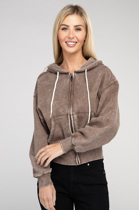 A smiling woman wearing a pink Acid Wash Cropped Zip-Up Hoodie and blue jeans, posing with one hand adjusting her hood.