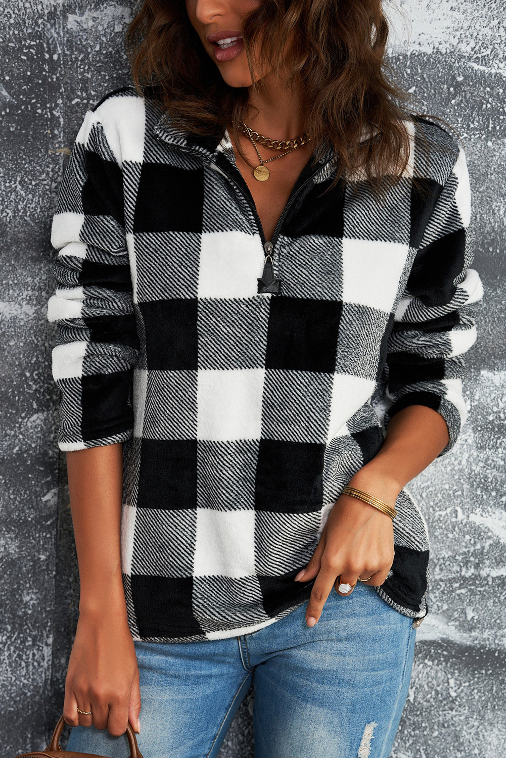 A woman with wavy hair is wearing a cozy Black Plaid Print 1/4 Zip Turn-down Collar Sweatshirt and blue jeans, standing with her back to the camera against a textured gray background.