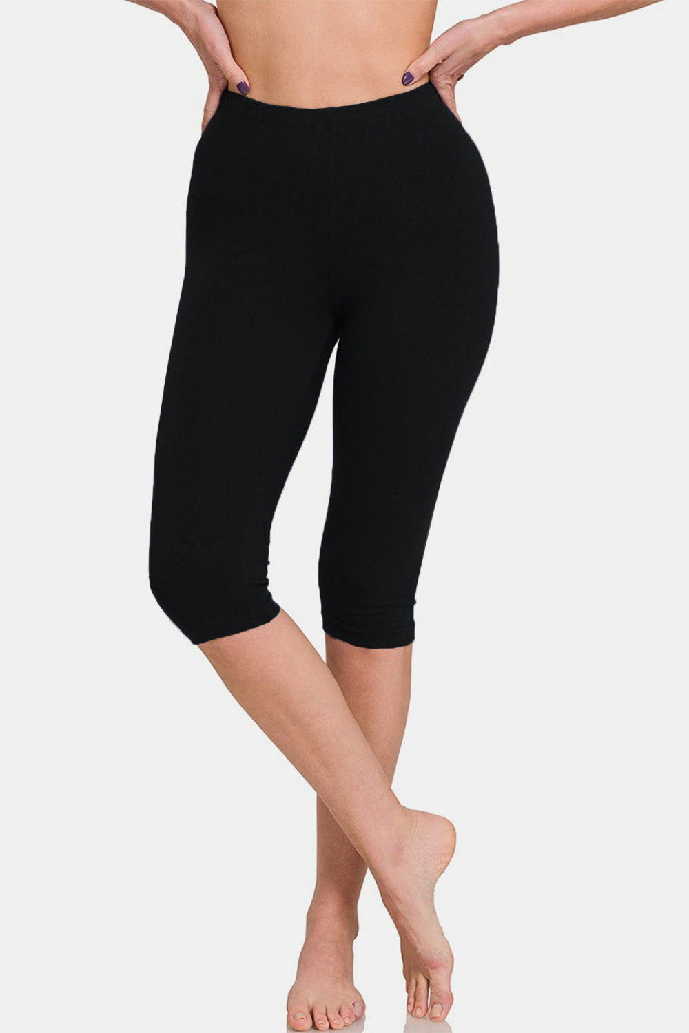 A person is standing barefoot wearing Zenana Full Size High Waist Capris, black knee-length leggings with a flattering fit, against a plain white background.