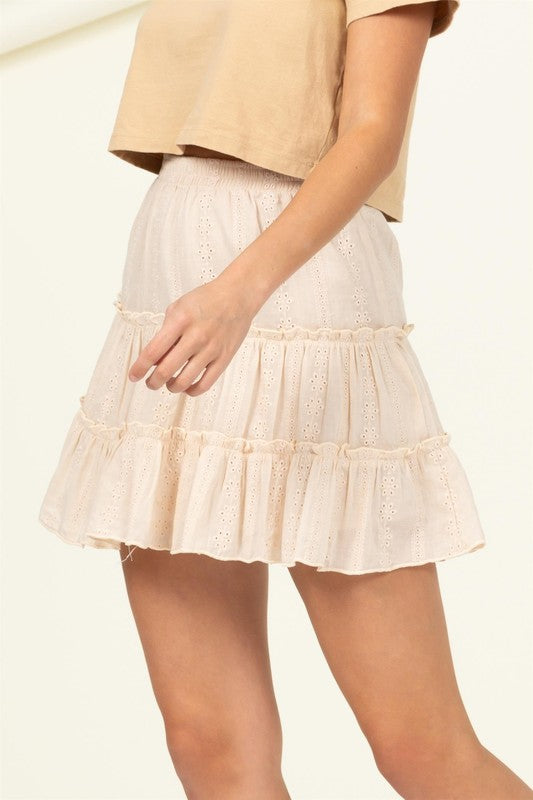 A person wearing the Forever Classy High Waist Tiered Mini Skirt in pink, featuring eyelet details and a ruffled design.