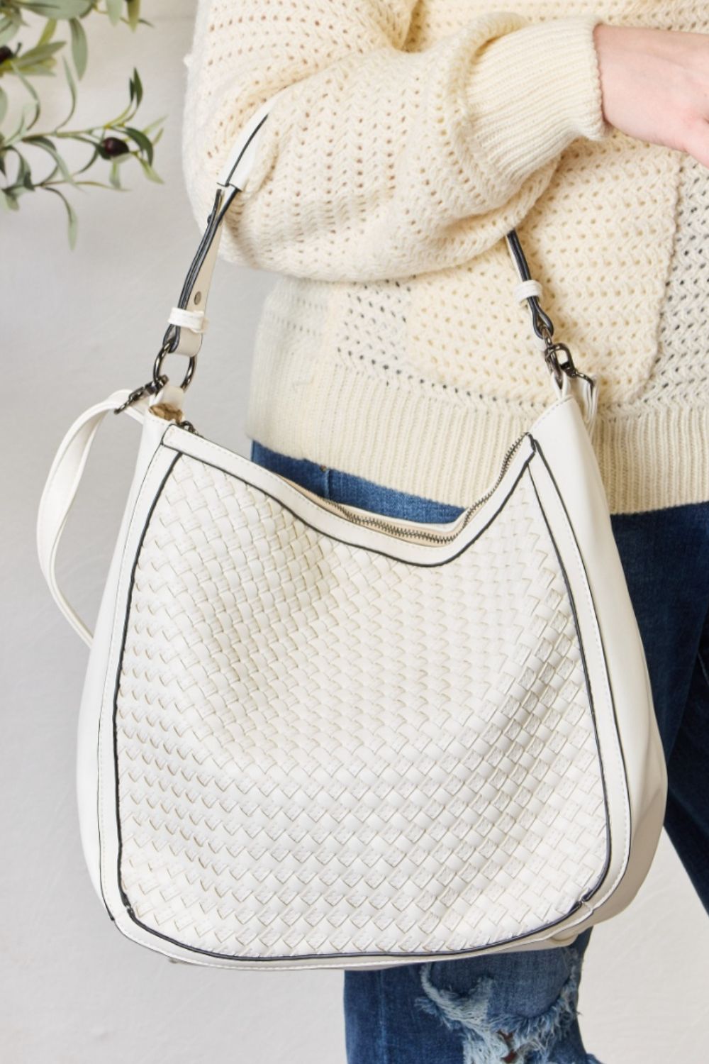 A person carries the SHOMICO Weaved Vegan Leather Handbag in a stylish brown hue, featuring a sleek crossbody strap, expertly paired with a cream sweater and jeans.