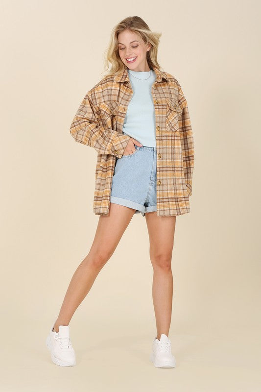 A person wearing the beige and brown Plaid shacket with pockets, featuring long sleeves and large buttons, holds the collar. Blonde hair is visible, adding a touch of elegance to the casual look.