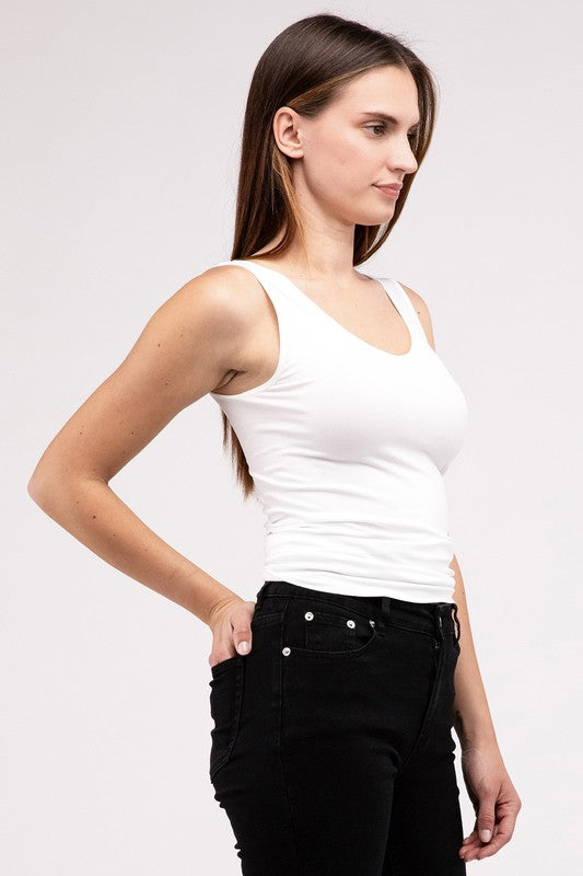 A woman in a white Front & Back 2-Way V-Neck Seamless Tank and black pants, standing with hands on hips and looking at the camera.