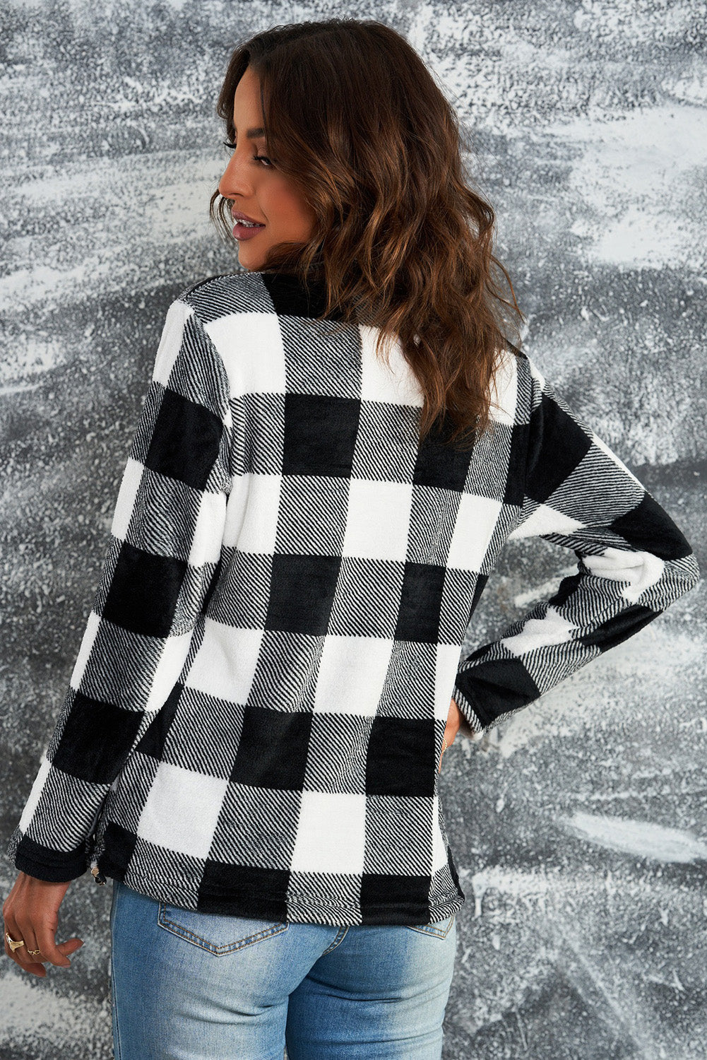 A woman with wavy hair is wearing a cozy Black Plaid Print 1/4 Zip Turn-down Collar Sweatshirt and blue jeans, standing with her back to the camera against a textured gray background.