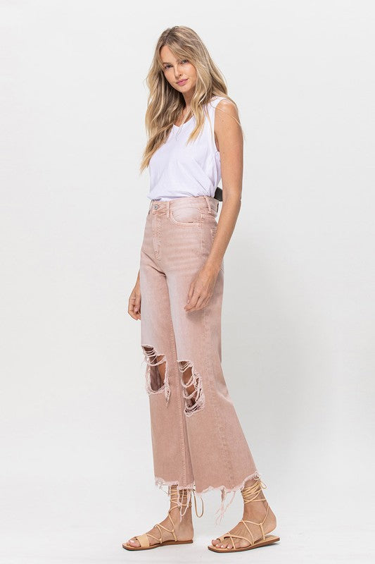 Person wearing 90's Vintage Crop Flare Jeans in rose pink with high waist, distressed details, rips on the knees, and frayed hems, paired with beige strappy sandals.