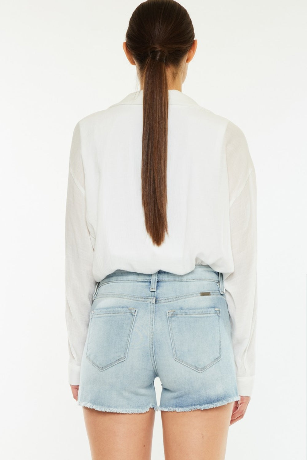 A person wearing a white shirt and the chic Kancan High Rise Side Slit Denim Shorts stands against a plain background, showcasing a perfect addition to any summer wardrobe.