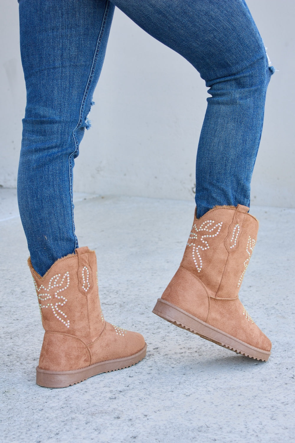 A person wearing ripped blue jeans and Forever Link Rhinestone Furry Flat Boots stands on a concrete surface.