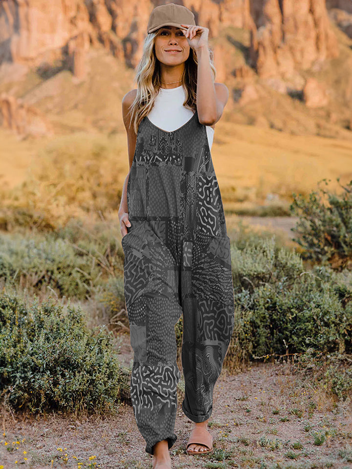 A person standing outdoors in front of rocky terrain, wearing a Full Size Printed V-Neck Sleeveless Jumpsuit and a hat.