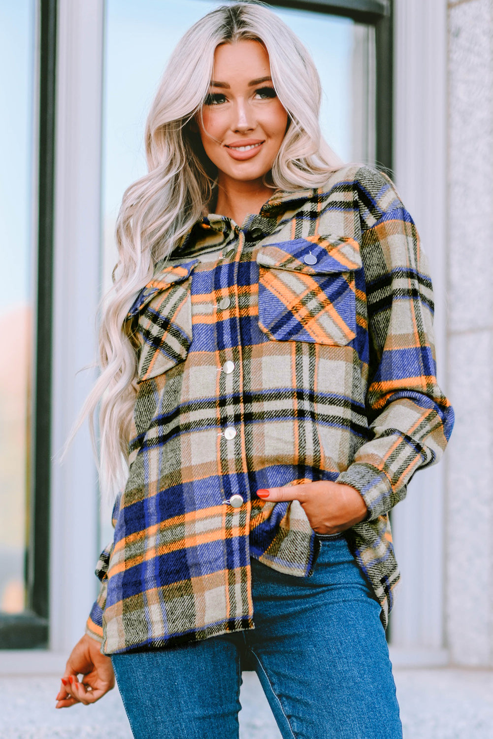 A person wearing a Brown Plaid Button Up Long Sleeve Flannel Shacket layered over a white top with ripped jeans and holding a brown handbag stands against a textured gray wall.