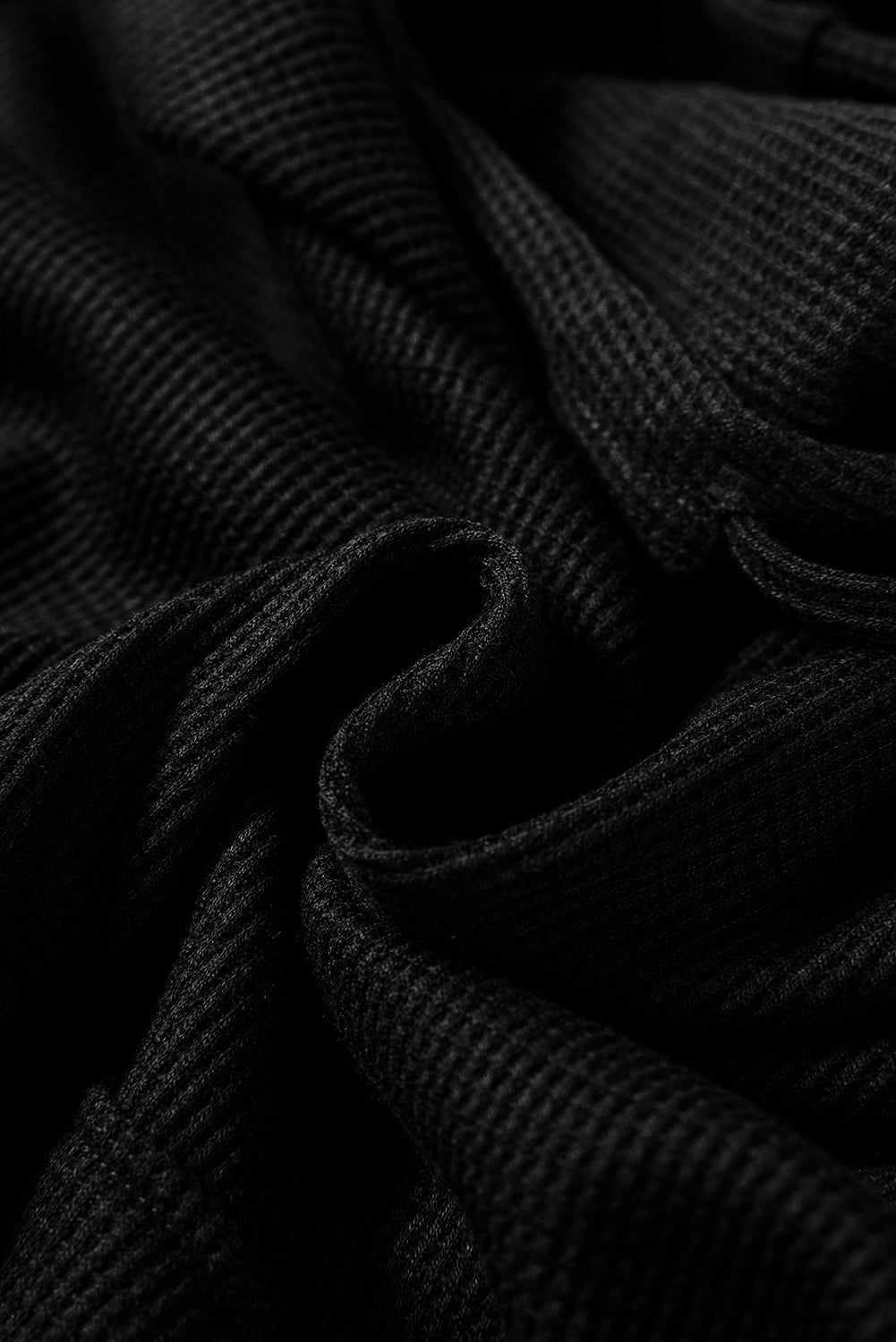 A woman wearing a Black Waffle Knit Fleece Lined High Low Oversized Hoodie and black shorts, standing and looking to the side against a plain background.