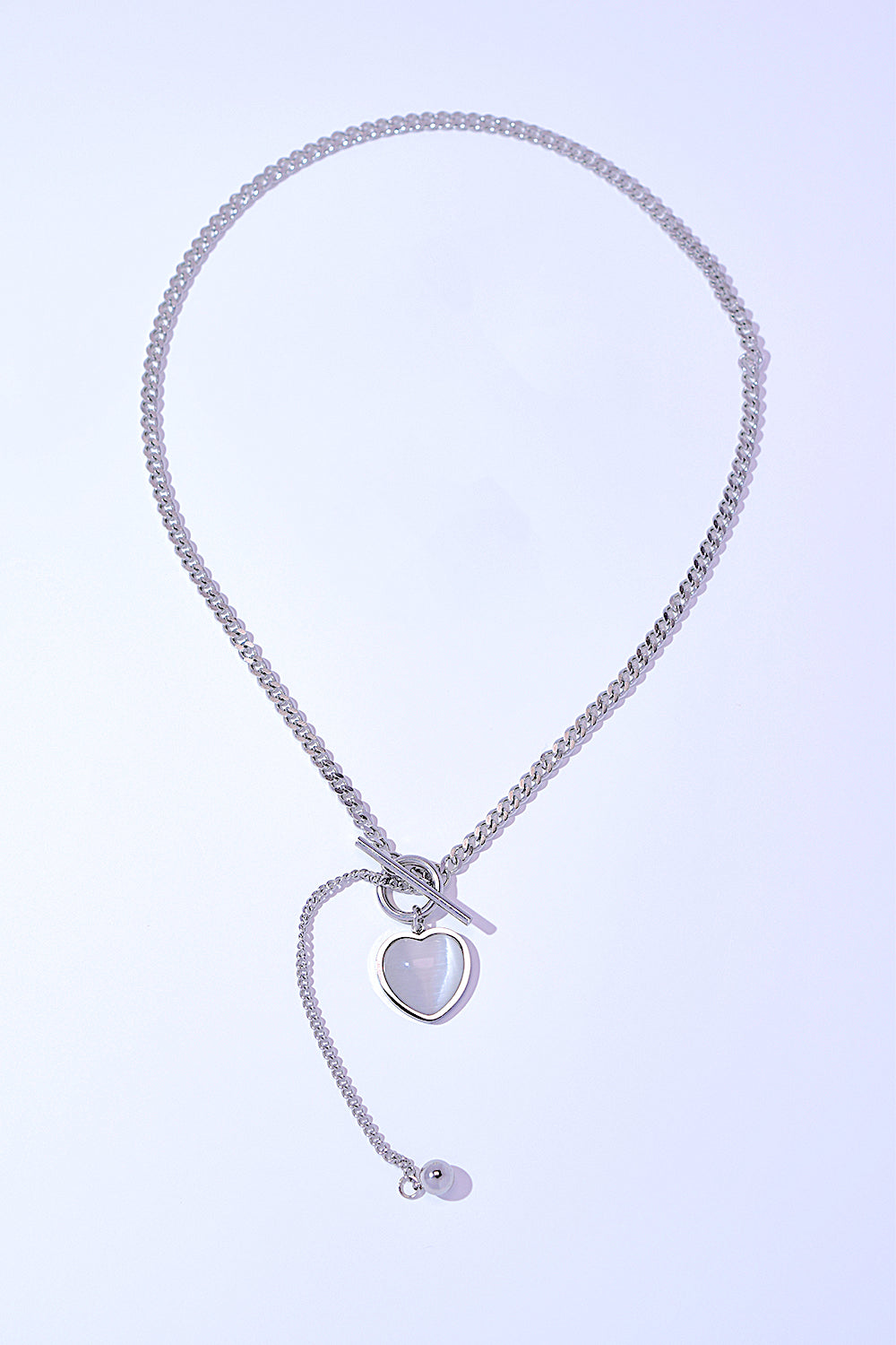 A Titanium Steel Heart Necklace with a heart-shaped pendant and a small key charm, featuring a delicate cat's eye stone, on a white background.