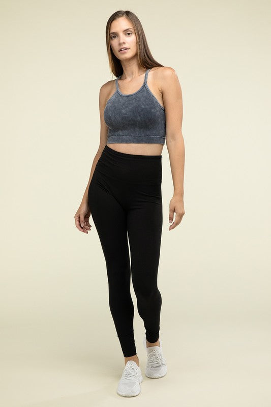 A person poses in a Washed Ribbed Seamless Cropped Cami Top with removable bra pads and black leggings against a neutral background.