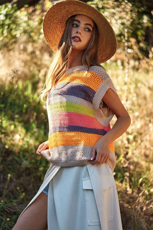 A woman outdoors wearing a Crochet Multi Striped Pullover Knit Sweater Vest and white pants, with her arms raised and eyes closed.